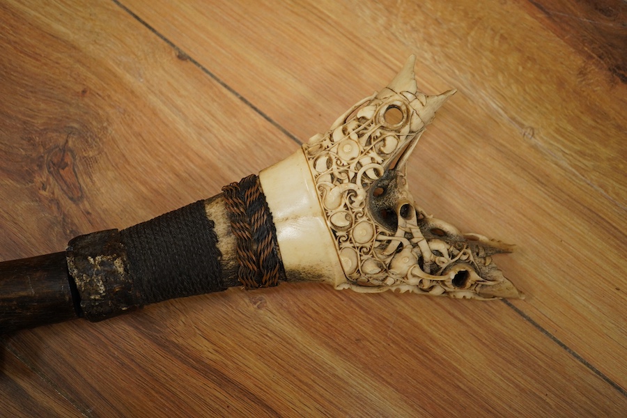 An elaborate Dayak headhunter’s sword Mandau, curved blade with chiselled and engraved back edge, large bone grip carved with protruding teeth, etc. in its wooden scabbard. Condition - good, some age wear.